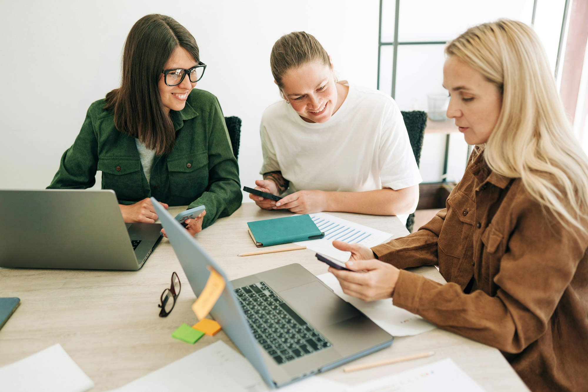 Female colleagues analyze social media marketing using mobile phone and laptops.