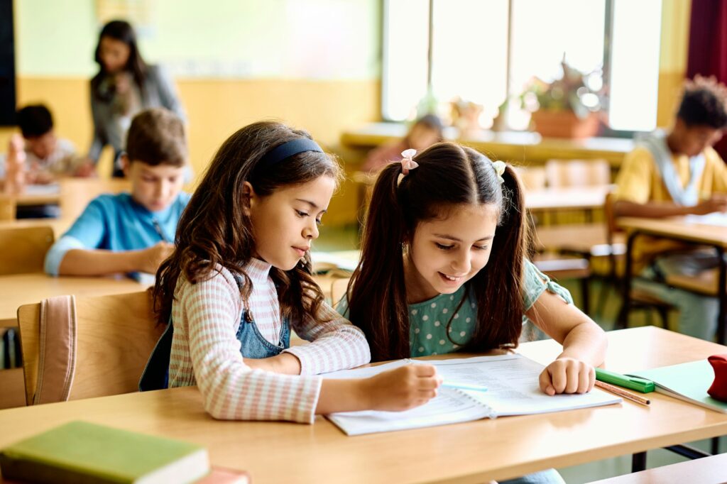 Happy schoolgirls learning together on a class at elementary school.