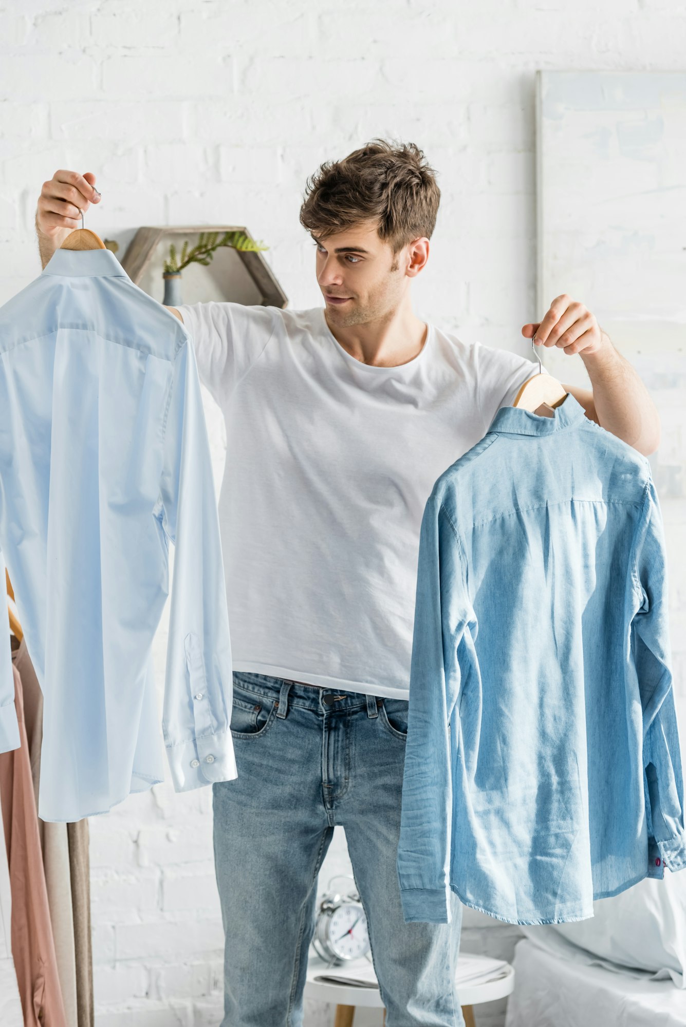 handsome man in white t-shirt holding shirts in bedroom