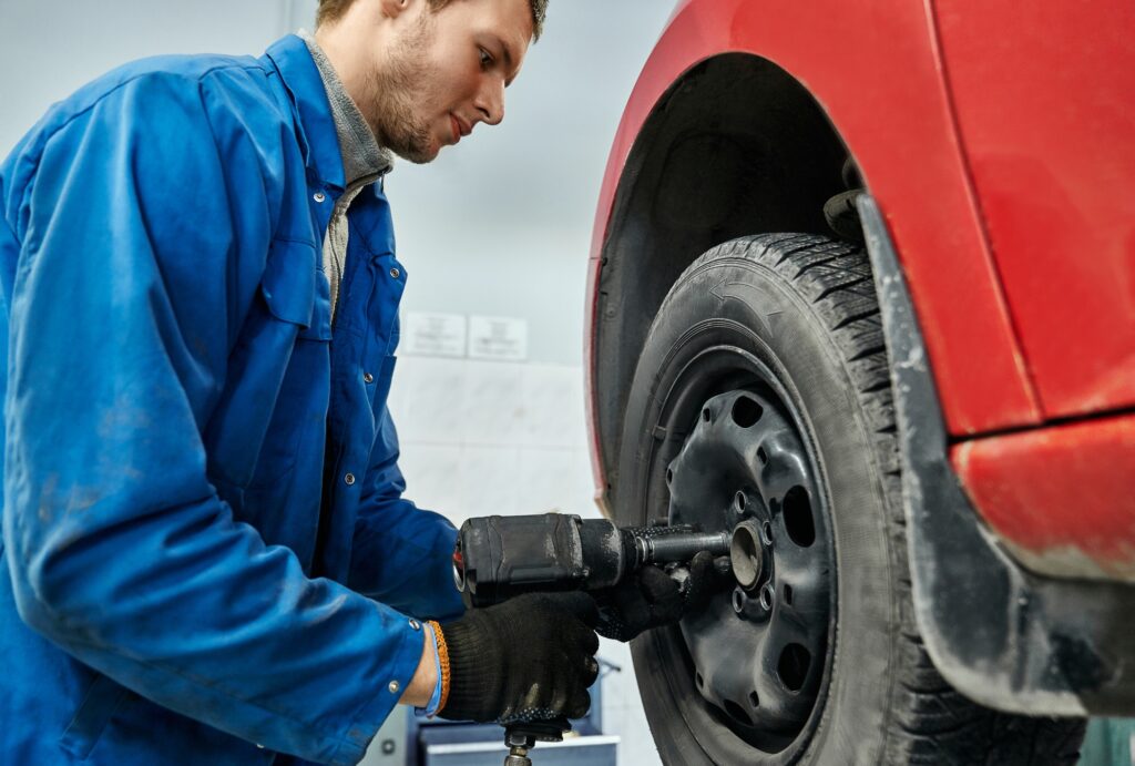 Auto mechanic changing car wheel with electric screwdriver