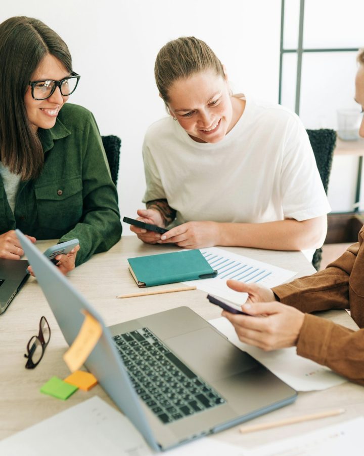 Female colleagues analyze social media marketing using mobile phone and laptops.